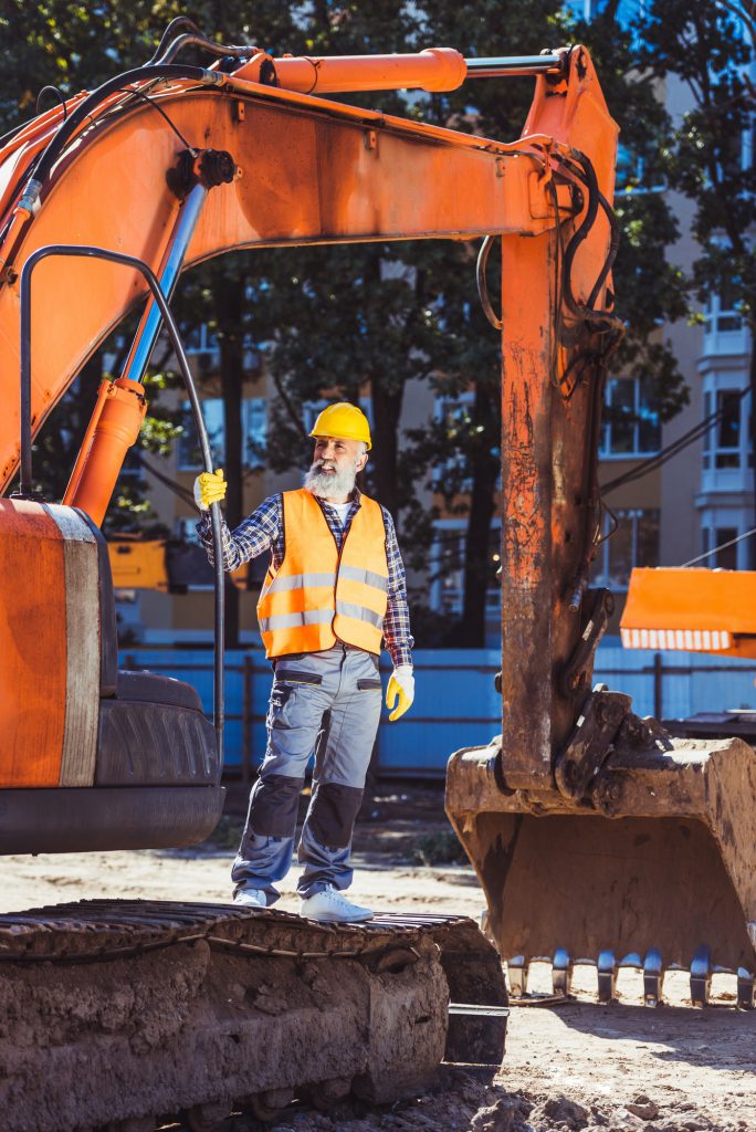 Worker in reflective vest and hardhat standing in front of excavator at construction site